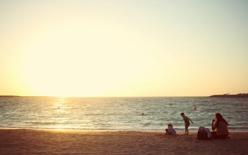 three people sitting near seashore during daytime
